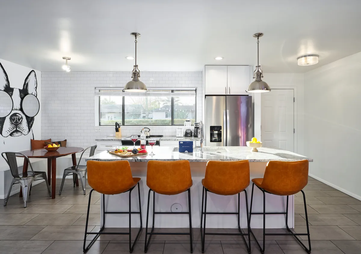 A focused view of the kitchen island bar with seating, highlighting the modern stainless steel appliances and the prominent dog mural on the wall. The space is styled for casual dining and entertaining, reinforcing the cheerful and relaxed vibe of the kitchen area.