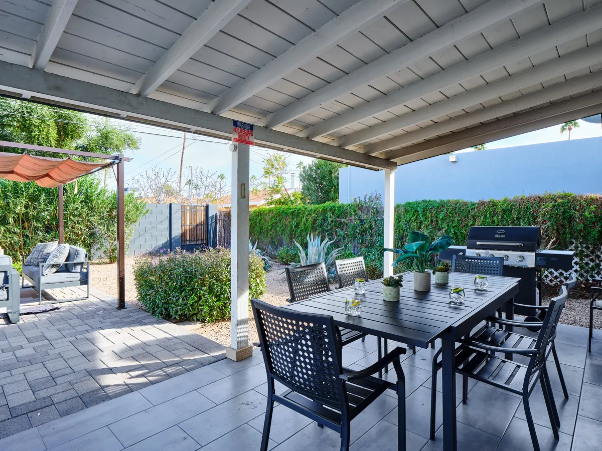 The image highlights an outdoor dining area featuring a table with chairs, a grill, and additional seating surrounded by greenery. The setting suggests a space perfect for socializing and enjoying meals al fresco.