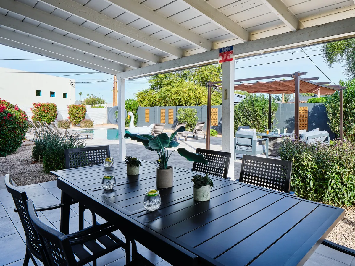 A relaxed outdoor dining area adjacent to a stylish swimming pool, surrounded by a landscaped garden. The space is set for gatherings with a dining table, comfortable chairs, and ample room for friends to lounge and enjoy the sunshine or evening ambiance.