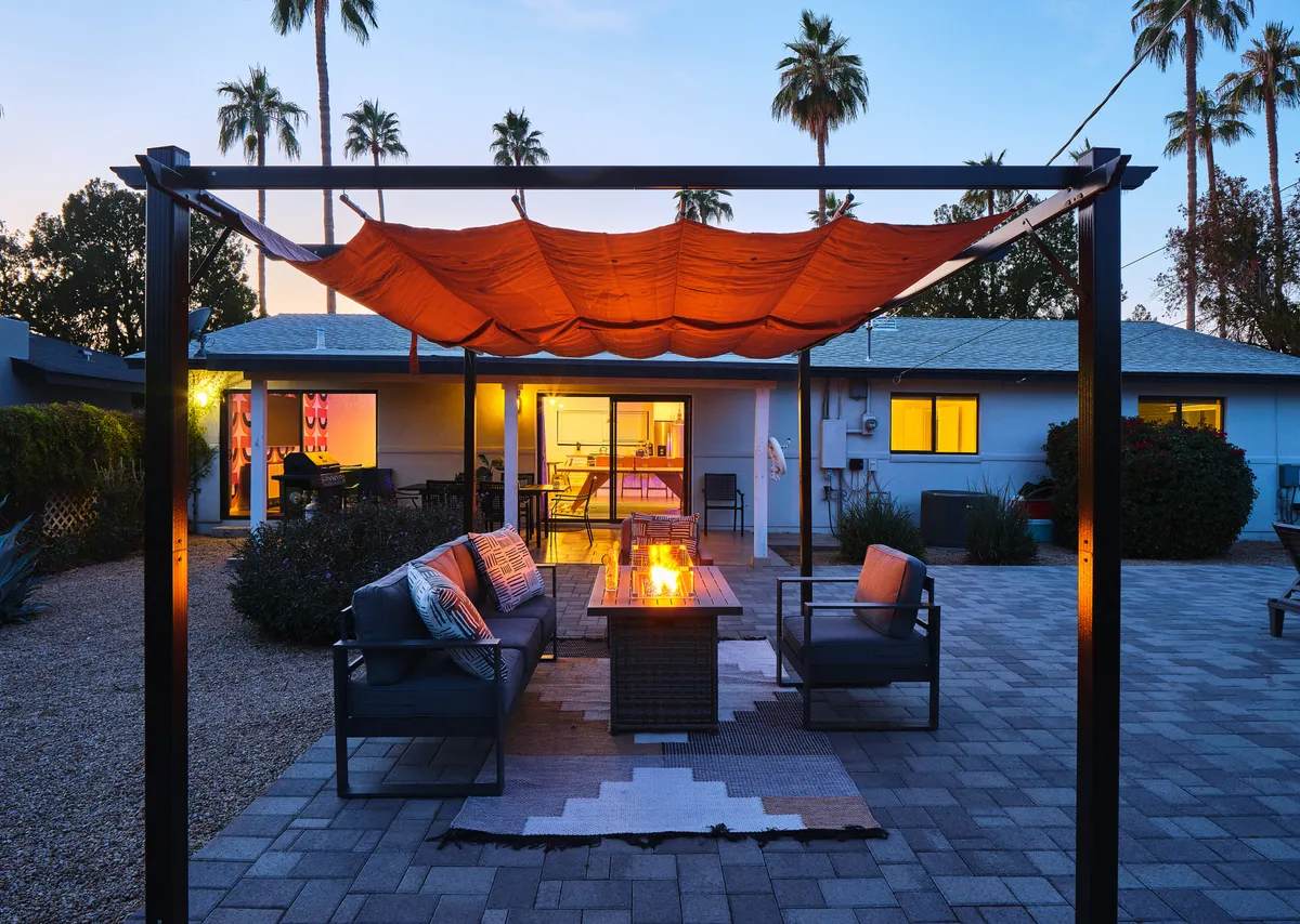 This image captures an outdoor seating area arranged around a glowing fire pit, framed by palm trees and illuminated windows. The scene is warm and social, suggesting memorable evenings spent outdoors.