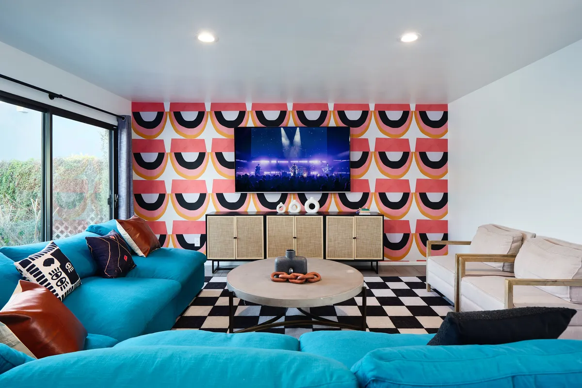 This image showcases a vibrant blue couch set against a colorful patterned wall, with a large flat-screen TV and a checkered coffee table at the center. The room is filled with energetic colors and retro-chic decor, evoking a playful, welcoming atmosphere perfect for social gatherings.