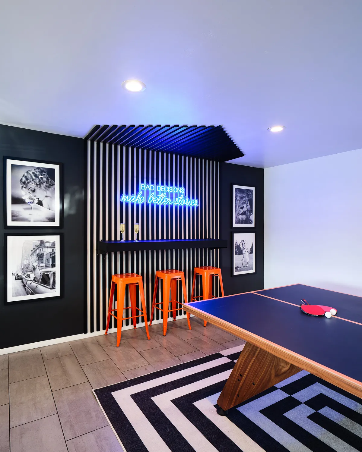 The game room features a ping pong table, neon sign lighting, bar stools, and black and white photography on the walls. The atmosphere is lively and designed for spontaneous fun and social interaction.