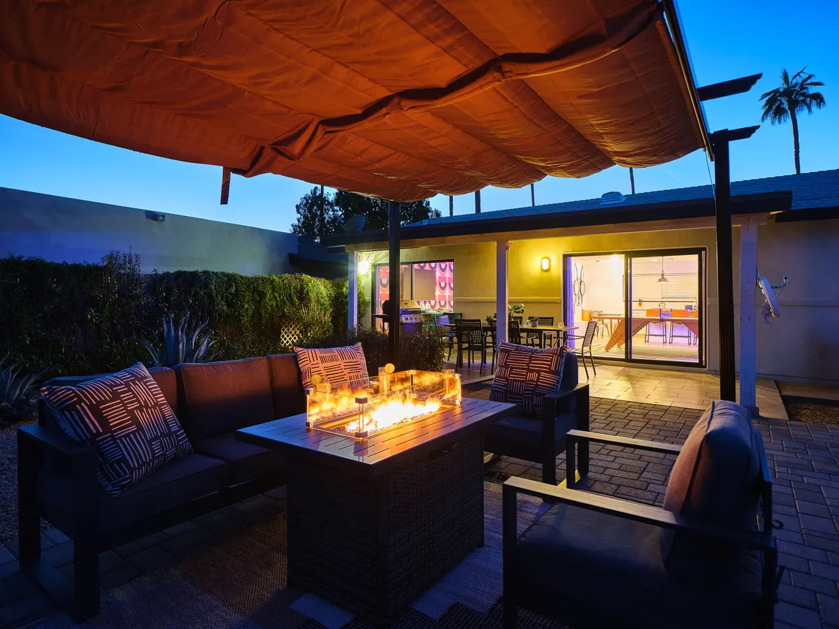 An inviting exterior area with a fire pit, comfortable seating, and an outdoor canopy, all framed by palm trees. The ambiance is intimate, ideal for evening conversations and relaxed gatherings under the stars.