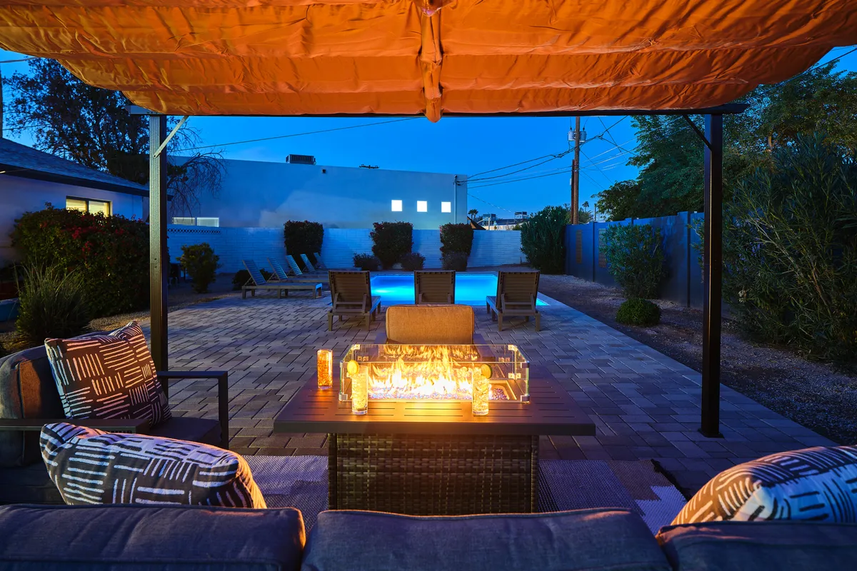 This nighttime exterior shot features a cozy fire pit surrounded by inviting seating and a sparkling swimming pool, creating a warm, intimate ambiance. The setting is perfect for unwinding after a night out, sharing stories with friends, and enjoying the Arizona evening.