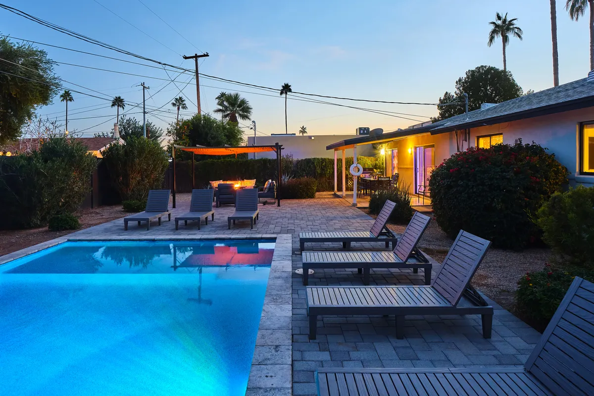 This image showcases the swimming pool lined with lounge chairs, a stylish fire pit area with ample seating, and a well-landscaped outdoor space. The overall scene is tranquil and social, perfect for daytime relaxation or evening gatherings.